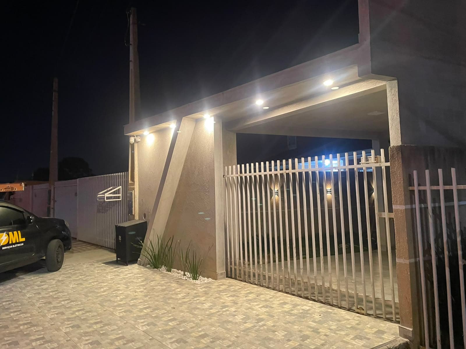 Fachada de residência à noite com iluminação embutida e spots de LED instalados pela DML, viatura da DML estacionada na garagem